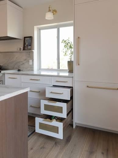Modern kitchen with white cabinetry, open drawers, and a large window above the counter with gold hardware and brass accents