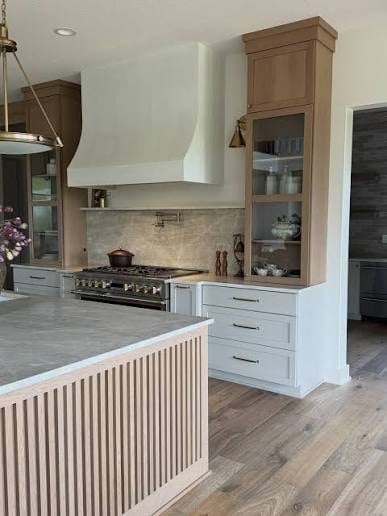 Modern kitchen with white hood vent, wood cabinetry, gas range, island with vertical slat detailing, and light wood flooring