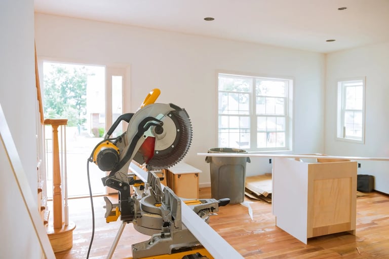Miter saw set up in a bright home interior with white walls, wooden flooring, and construction materials