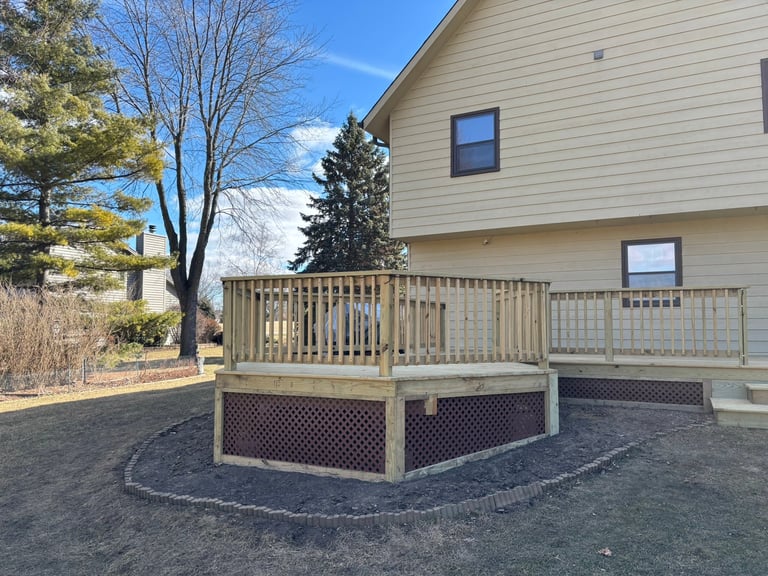 Two-story beige house with wooden deck and lattice skirting in a residential yard with bare trees