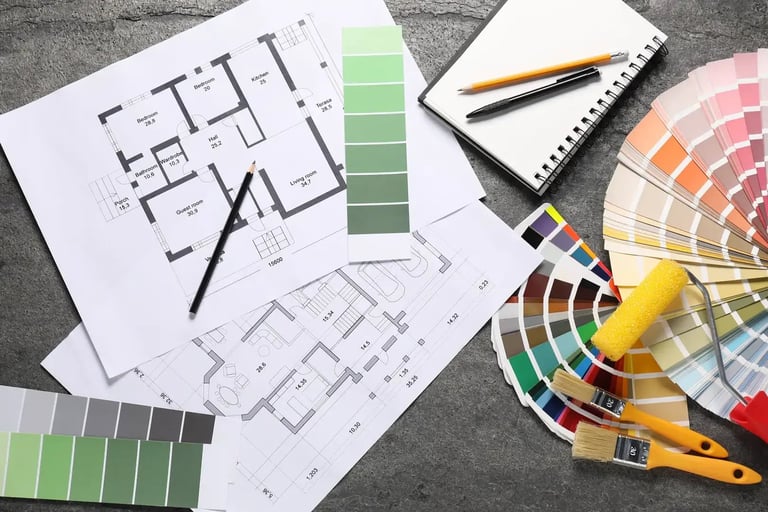Interior design workspace with architectural floor plans, paint color swatches, color wheel, brush, and notebook on gray surface