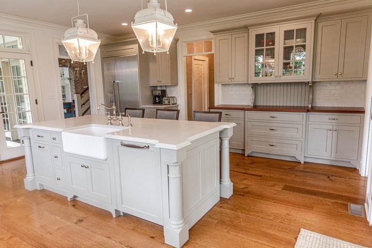 Modern kitchen with white cabinetry, large island with farmhouse sink, pendant lights, stainless steel appliances, and hardwood flooring