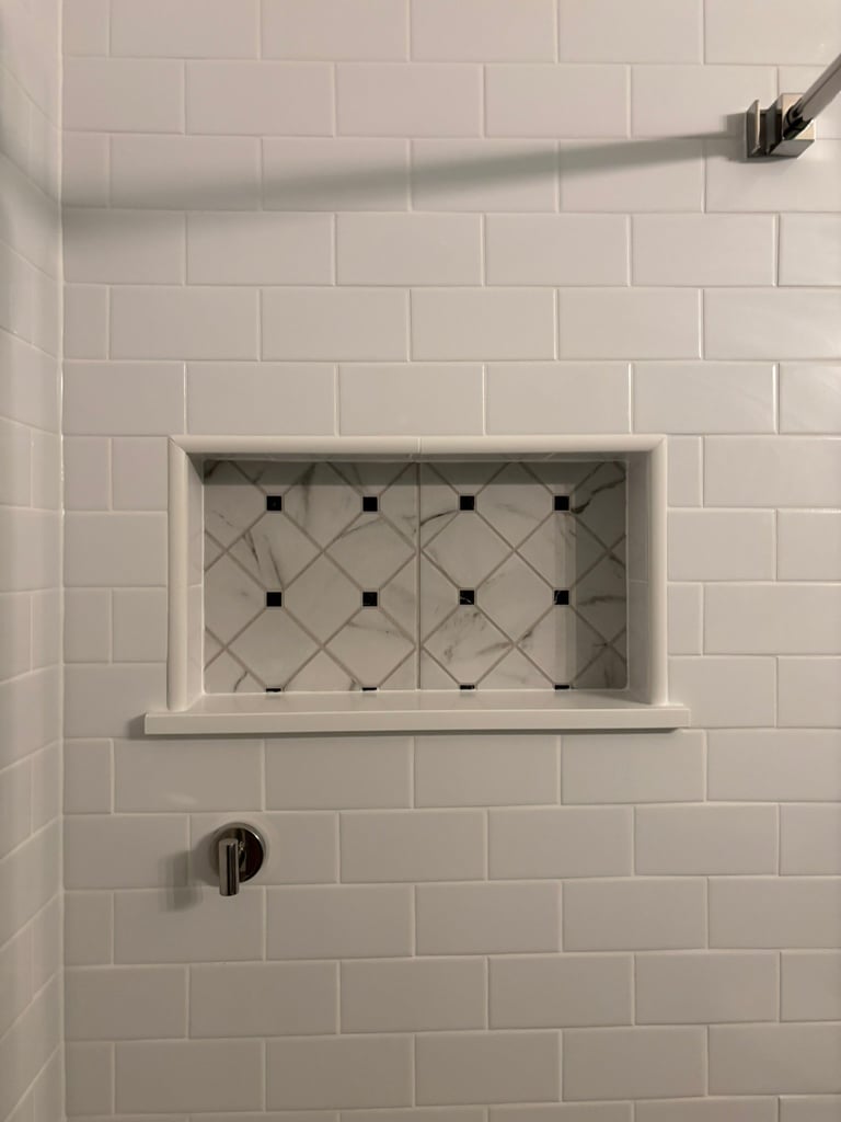 White subway tile shower wall with recessed niche containing black and white geometric patterned tiles, chrome fixtures visible